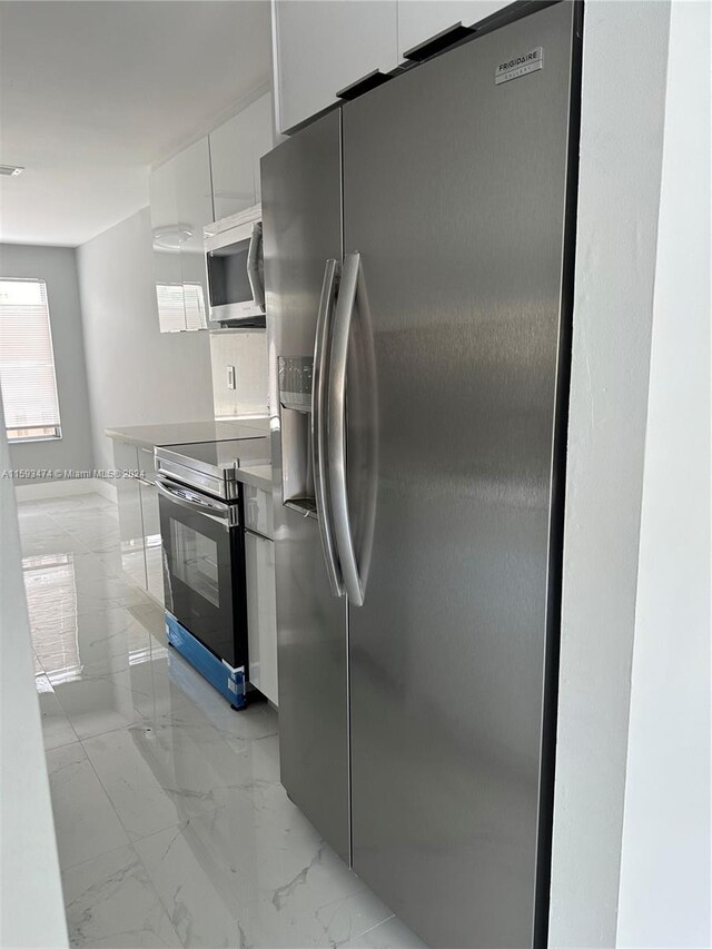 kitchen with appliances with stainless steel finishes, light tile patterned flooring, and white cabinets