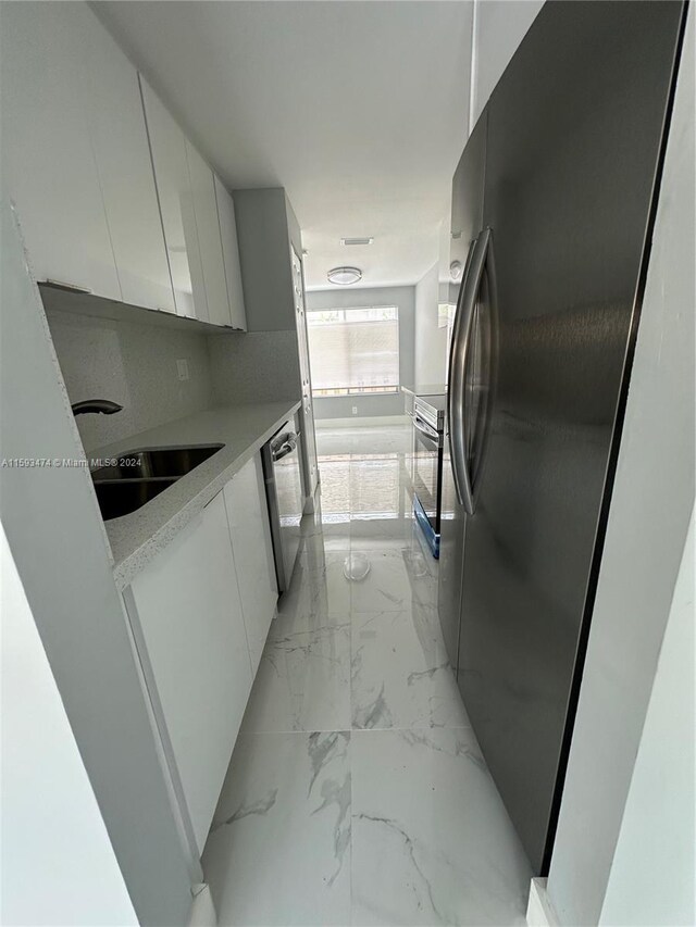 kitchen with white cabinetry, stainless steel dishwasher, black fridge, decorative backsplash, and sink