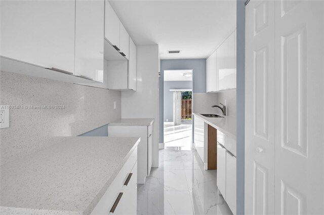 kitchen featuring sink, light stone counters, backsplash, light tile patterned floors, and white cabinetry