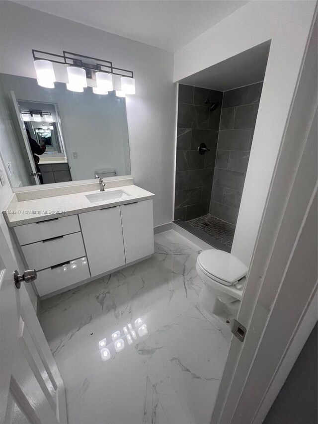 bathroom with tiled shower, vanity, tile patterned flooring, and toilet