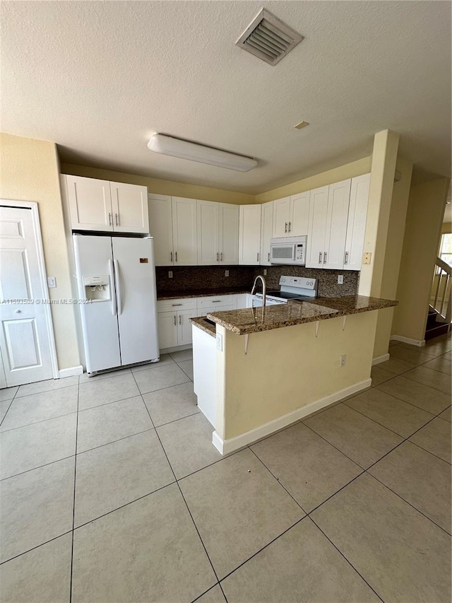 kitchen featuring a breakfast bar, kitchen peninsula, white appliances, and white cabinetry