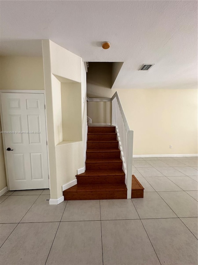 staircase featuring light tile flooring and a textured ceiling