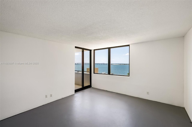 empty room with a textured ceiling, concrete flooring, and a water view