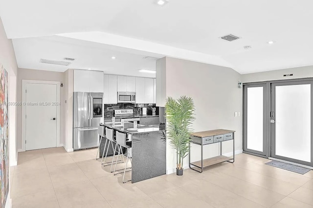 kitchen with appliances with stainless steel finishes, tasteful backsplash, white cabinetry, lofted ceiling, and a breakfast bar area