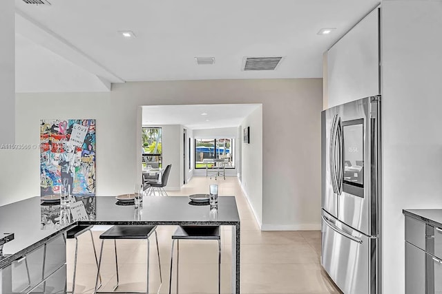 kitchen with stainless steel refrigerator, white cabinetry, dark stone counters, and light tile patterned flooring