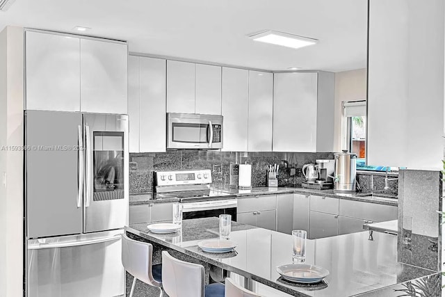 kitchen featuring white cabinetry, tasteful backsplash, dark stone counters, a kitchen breakfast bar, and stainless steel appliances