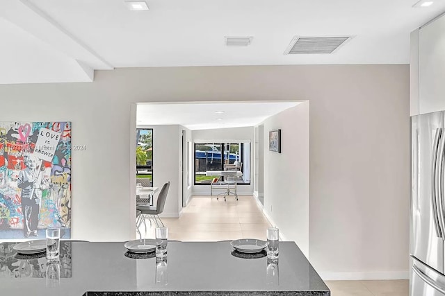 interior space featuring stainless steel refrigerator, dark stone countertops, light tile patterned floors, and white cabinets