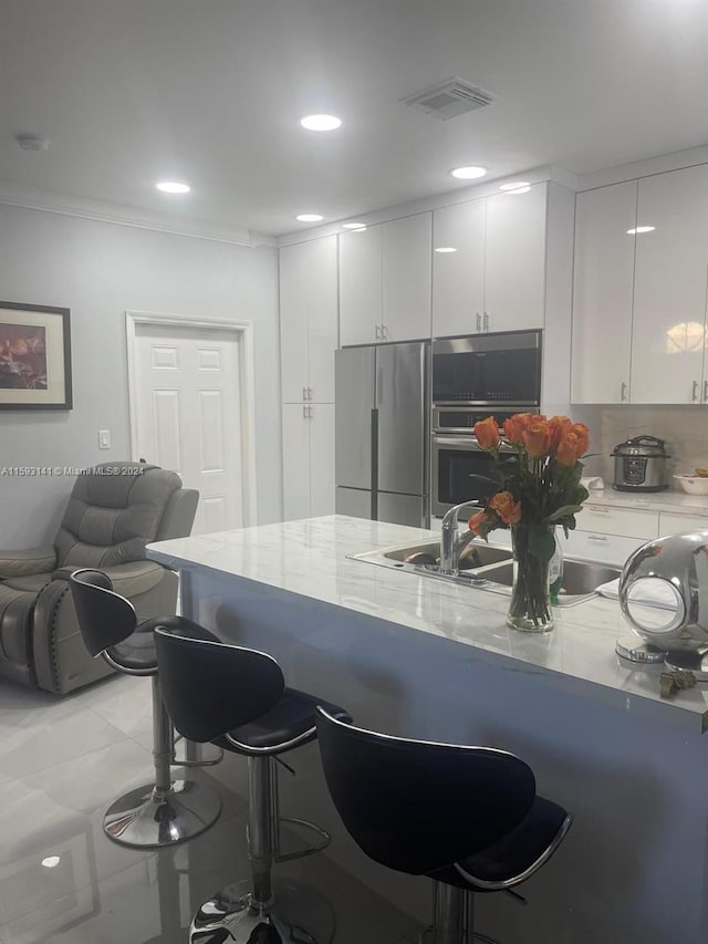 kitchen featuring a kitchen breakfast bar, stainless steel appliances, white cabinetry, and light tile floors