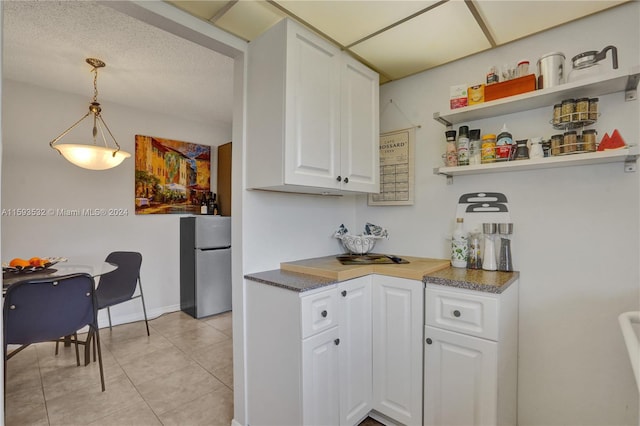 kitchen with stainless steel refrigerator, light tile flooring, white cabinets, a textured ceiling, and pendant lighting