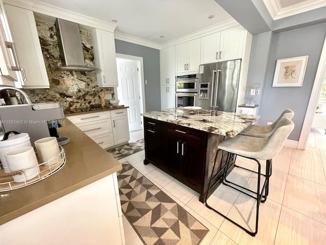 kitchen with wall chimney range hood, white cabinetry, stainless steel appliances, crown molding, and a center island