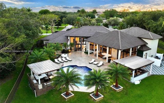 back house at dusk with outdoor lounge area, a patio area, a yard, a fenced in pool, and area for grilling