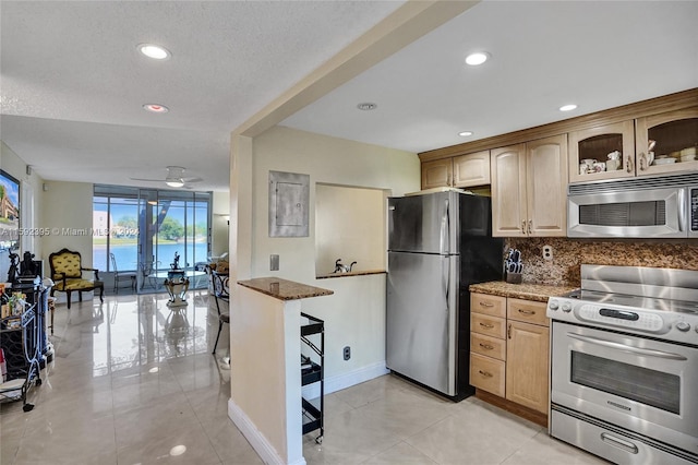 kitchen with ceiling fan, a water view, stone counters, backsplash, and appliances with stainless steel finishes