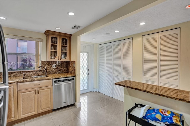 kitchen featuring dark stone counters, light tile flooring, dishwasher, tasteful backsplash, and sink