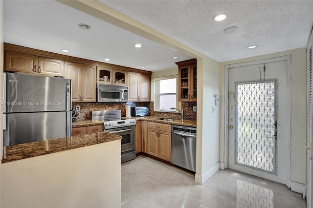 kitchen with dark stone counters, backsplash, light tile floors, sink, and appliances with stainless steel finishes