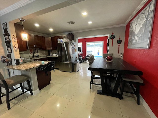 kitchen featuring crown molding, a breakfast bar area, stainless steel refrigerator with ice dispenser, light stone countertops, and decorative light fixtures