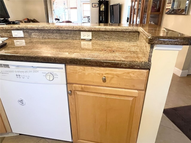 kitchen with dishwasher, dark stone counters, light brown cabinetry, and tile floors