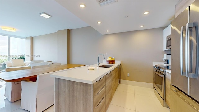 kitchen featuring an island with sink, sink, light tile patterned floors, and stainless steel appliances