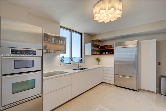 kitchen with built in fridge, white cabinetry, black electric stovetop, double oven, and sink