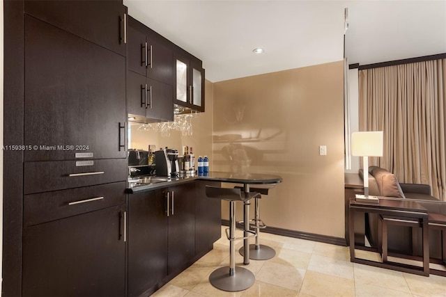 bar with dark brown cabinetry, sink, and light tile flooring