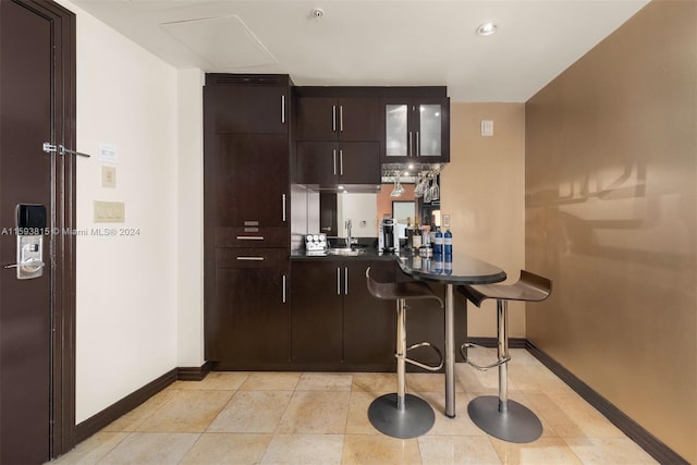 kitchen with dark brown cabinets, a kitchen breakfast bar, kitchen peninsula, light tile flooring, and sink