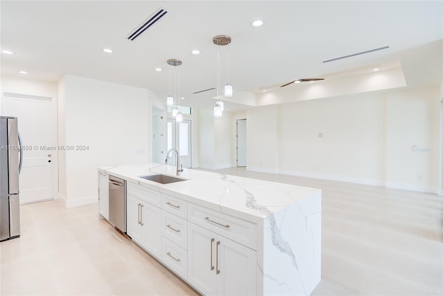 kitchen with an island with sink, sink, white cabinets, hanging light fixtures, and light stone countertops