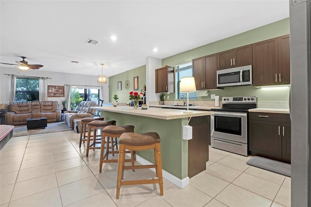 kitchen featuring dark brown cabinetry, stainless steel appliances, a kitchen breakfast bar, pendant lighting, and a center island with sink