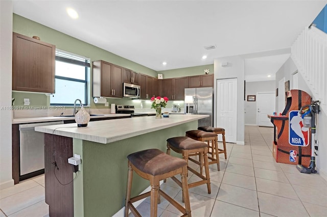 kitchen with stainless steel appliances, sink, light tile patterned floors, a center island, and a breakfast bar area