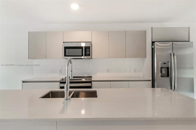 kitchen with stainless steel appliances, gray cabinets, light stone counters, and tasteful backsplash