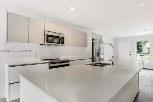 kitchen with light tile flooring, stainless steel appliances, tasteful backsplash, a kitchen island with sink, and light stone countertops