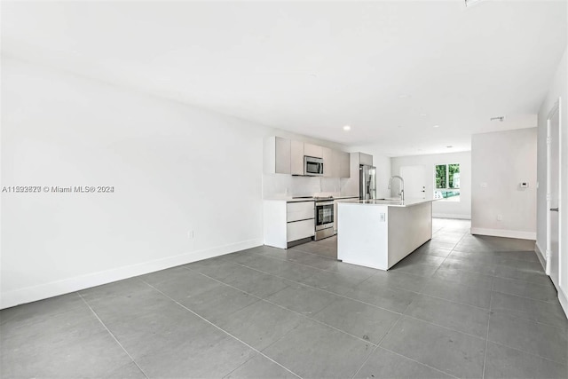 kitchen featuring a center island with sink, stainless steel appliances, tile floors, sink, and white cabinetry