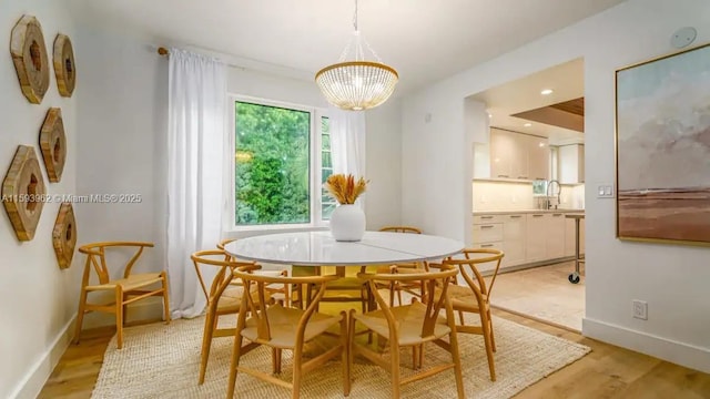 dining area featuring a notable chandelier, sink, and light hardwood / wood-style flooring