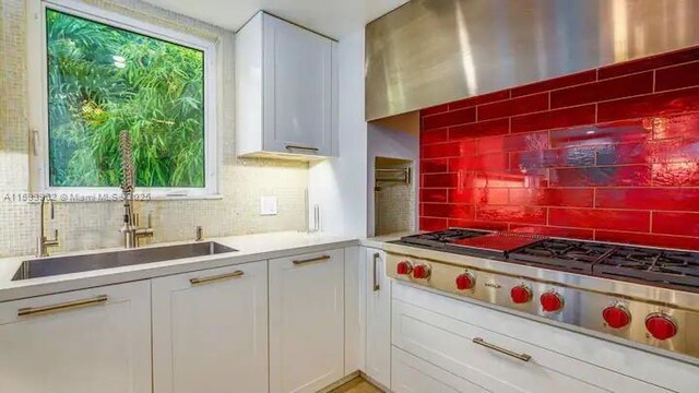 kitchen featuring decorative backsplash, stainless steel gas cooktop, sink, and white cabinets