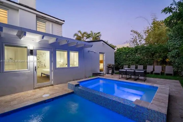 pool at dusk featuring an in ground hot tub and a patio