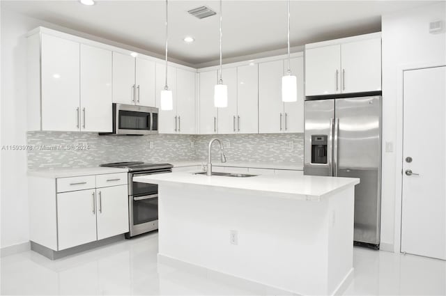 kitchen with stainless steel appliances, white cabinetry, hanging light fixtures, sink, and a kitchen island with sink