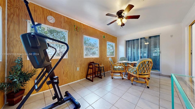 exercise room with a wealth of natural light, wood walls, light tile patterned flooring, and ceiling fan