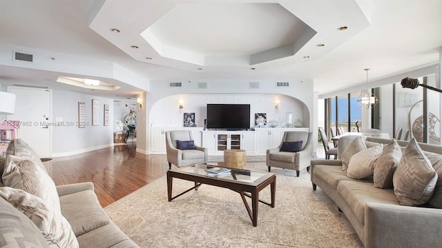 living room with a notable chandelier, hardwood / wood-style flooring, and a raised ceiling