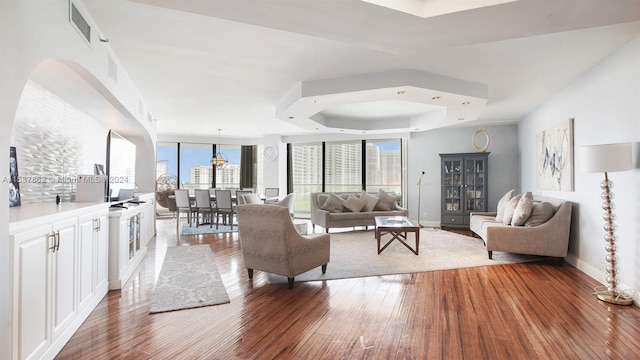 living room with a raised ceiling, an inviting chandelier, and hardwood / wood-style flooring