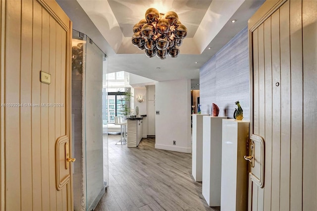 hallway featuring a notable chandelier, a tray ceiling, and light wood-type flooring