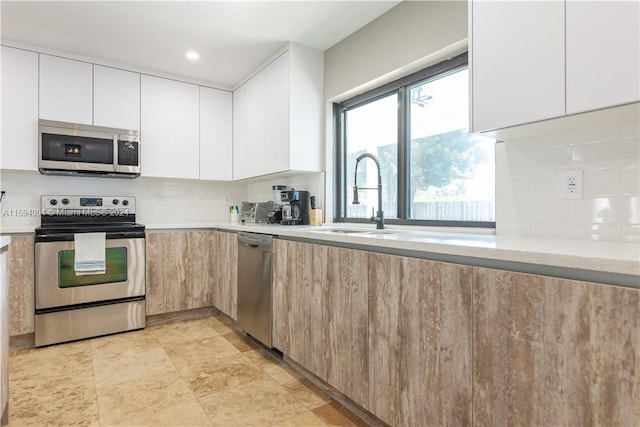 kitchen featuring sink, stainless steel appliances, light tile flooring, and white cabinetry