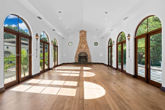 unfurnished living room featuring light wood-type flooring, french doors, high vaulted ceiling, and a fireplace