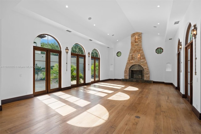 unfurnished living room with a stone fireplace, high vaulted ceiling, french doors, and wood-type flooring