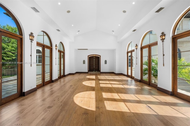 foyer with high vaulted ceiling, light hardwood / wood-style floors, french doors, and a healthy amount of sunlight