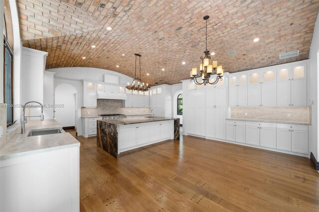 kitchen with hanging light fixtures, white cabinets, brick ceiling, backsplash, and sink