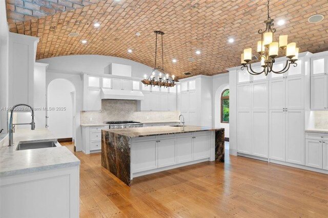 kitchen featuring light hardwood / wood-style floors, brick ceiling, tasteful backsplash, white cabinets, and pendant lighting