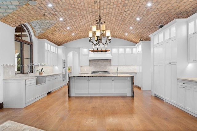 kitchen with brick ceiling, light wood-type flooring, backsplash, sink, and white cabinets