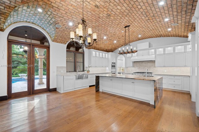 kitchen featuring backsplash, a center island with sink, hanging light fixtures, and brick ceiling