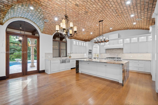 kitchen with light hardwood / wood-style flooring, an island with sink, hanging light fixtures, and brick ceiling