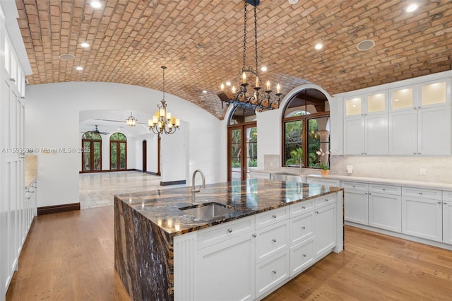 kitchen with dark stone counters, light hardwood / wood-style floors, brick ceiling, sink, and a kitchen island with sink