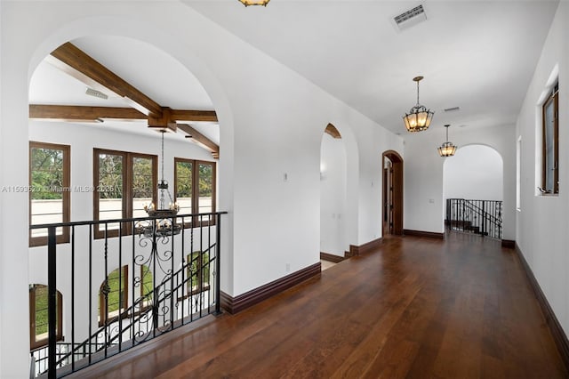 unfurnished room with beam ceiling, plenty of natural light, dark wood-type flooring, and an inviting chandelier