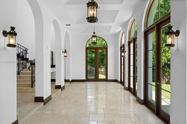 tiled entryway with coffered ceiling, a towering ceiling, and french doors